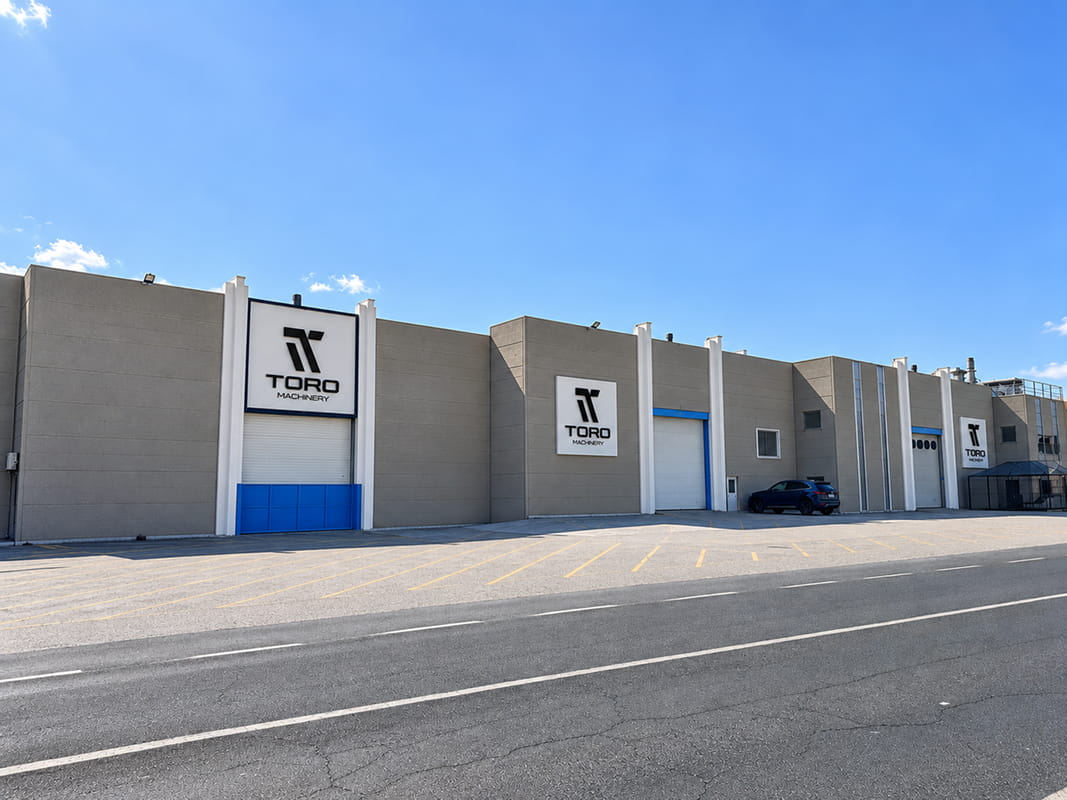 Fachada de un edificio industrial gris con tres rótulos blancos con el logotipo "TORO Machinery"